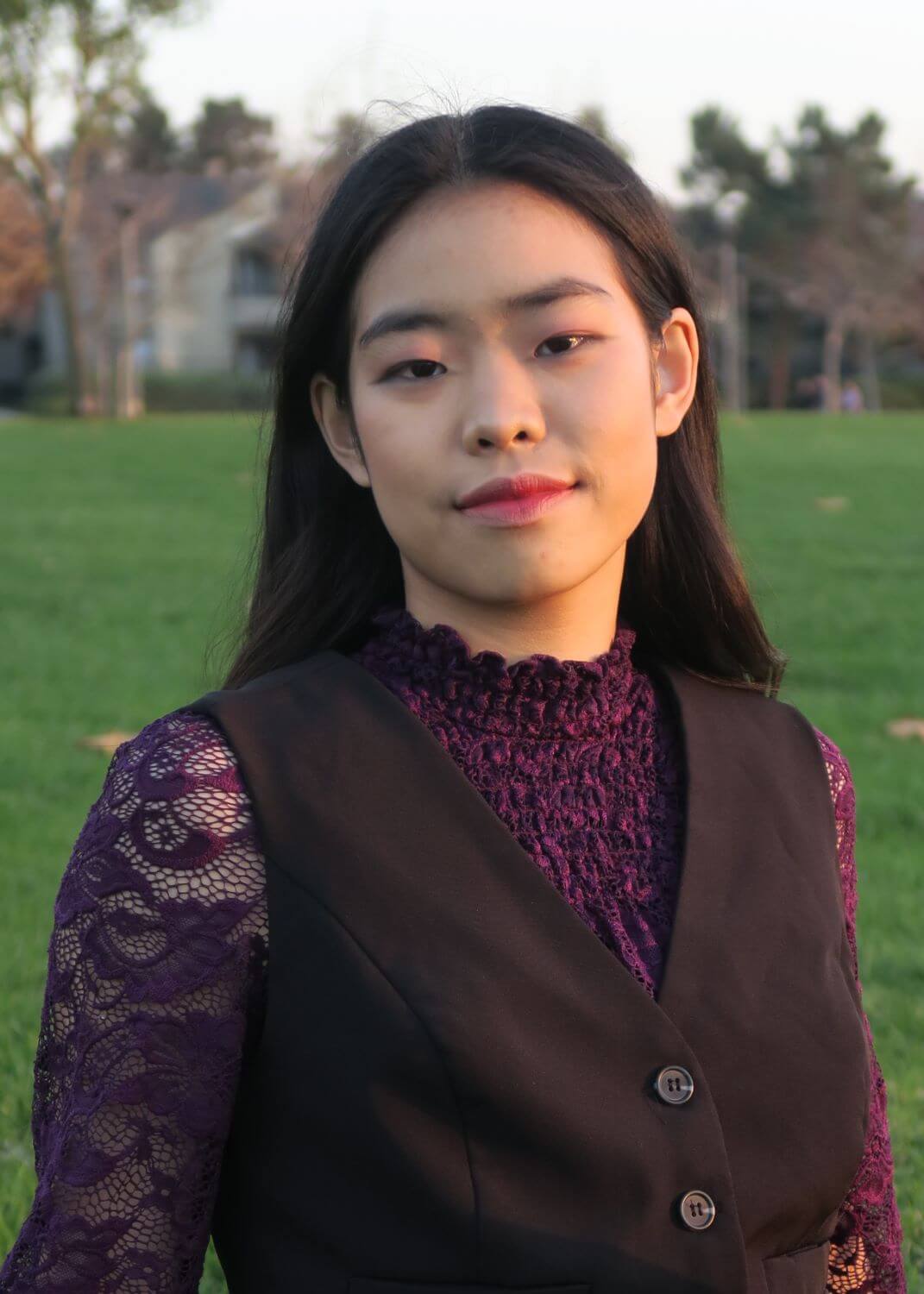 Lacole Yang from head to elbows. Lacole is a Chinese youth with dark hair and eyes. They are smiling. They are wearing a purple blouse and black vest.